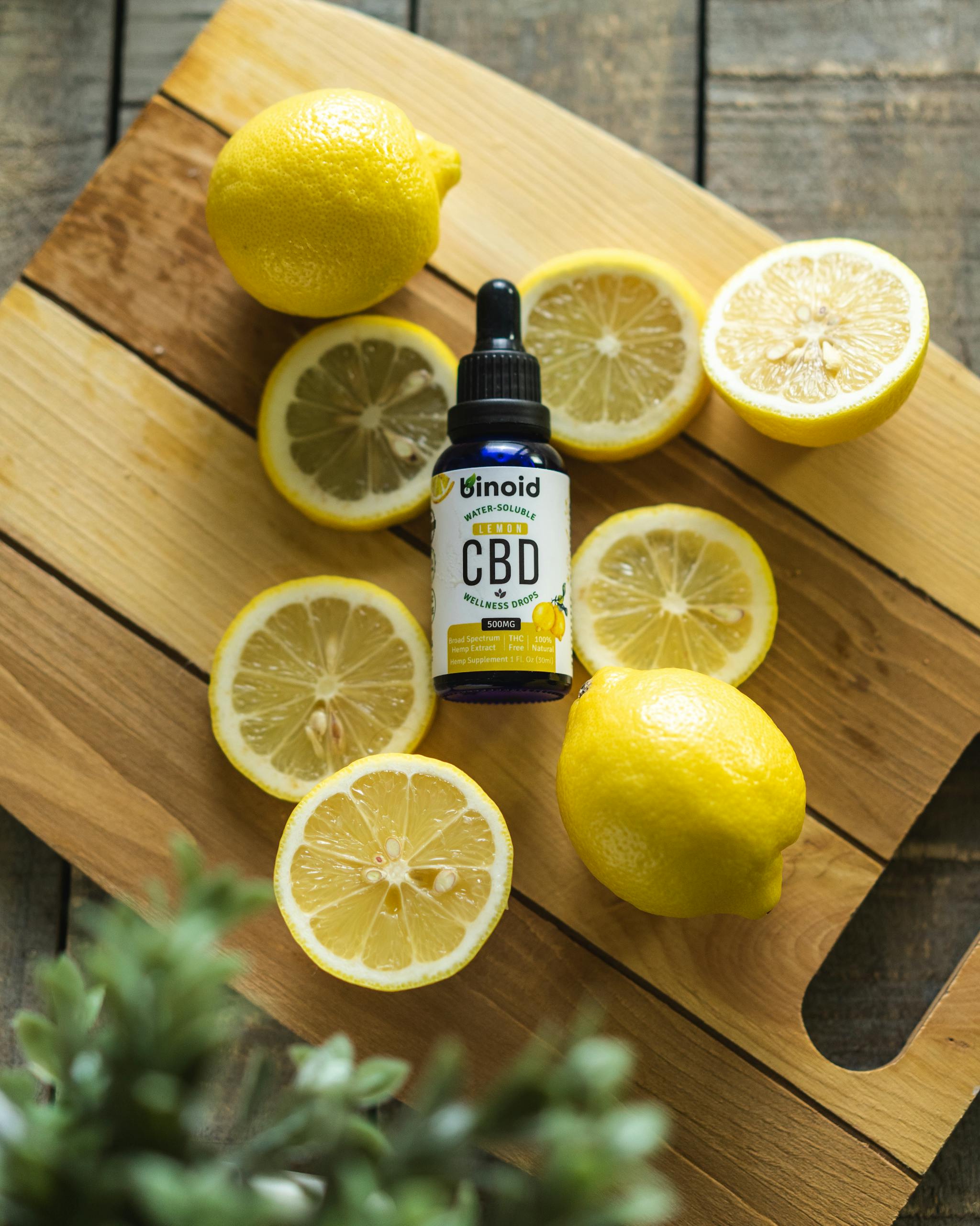 Top view of sliced fresh lemons surrounding a bottle of CBD oil on a rustic wooden board.